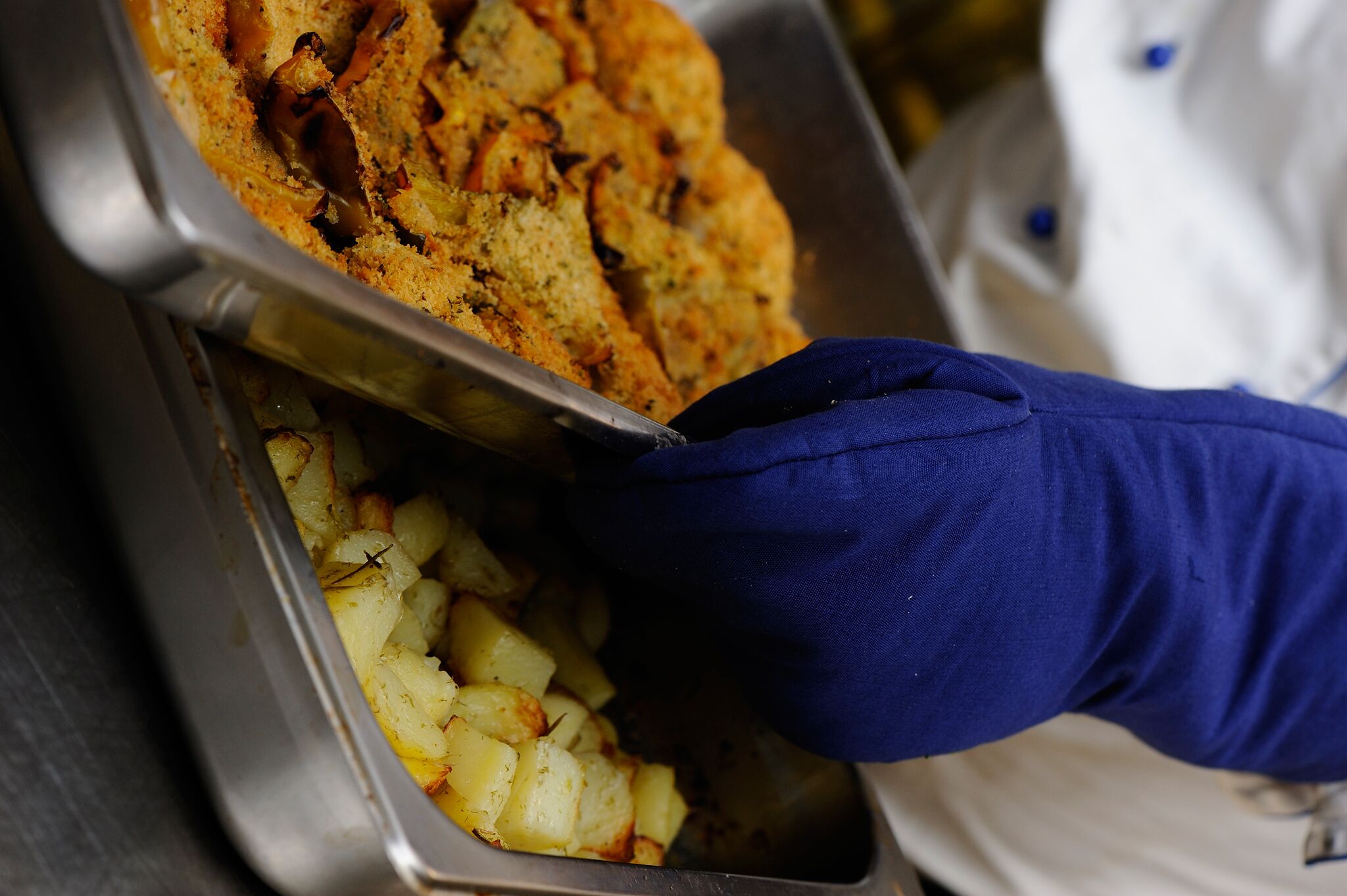 A person wearing a blue glove using tongs to serve food from a metal tray.