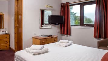 A hotel room with a bed, a TV, a wooden dresser, and a window with curtains.