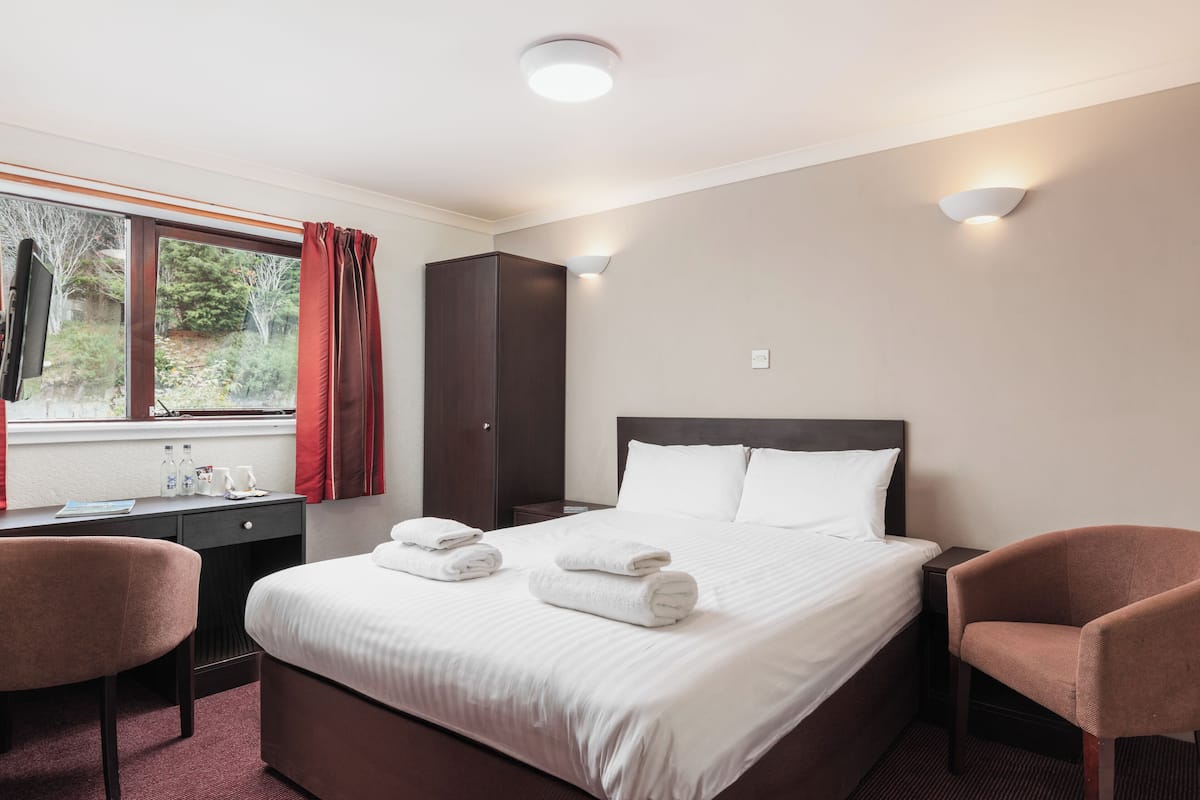 A hotel room with a large bed, two chairs, a desk, and a wardrobe.