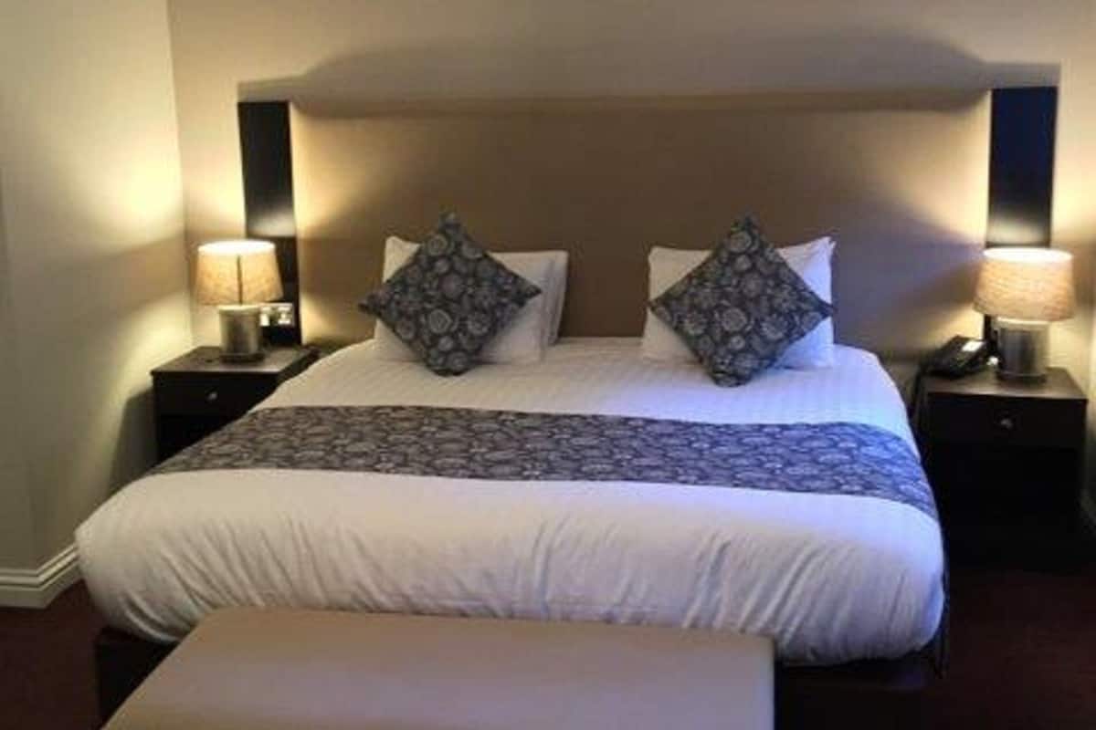 A neatly made bed with a patterned bedspread, two pillows, and a bedside table with a lamp.