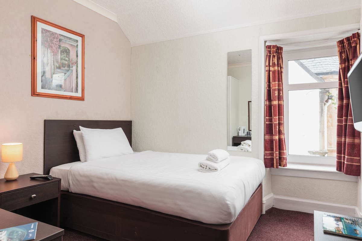A hotel room with a bed, a nightstand, a lamp, a window with curtains, and a framed picture on the wall.