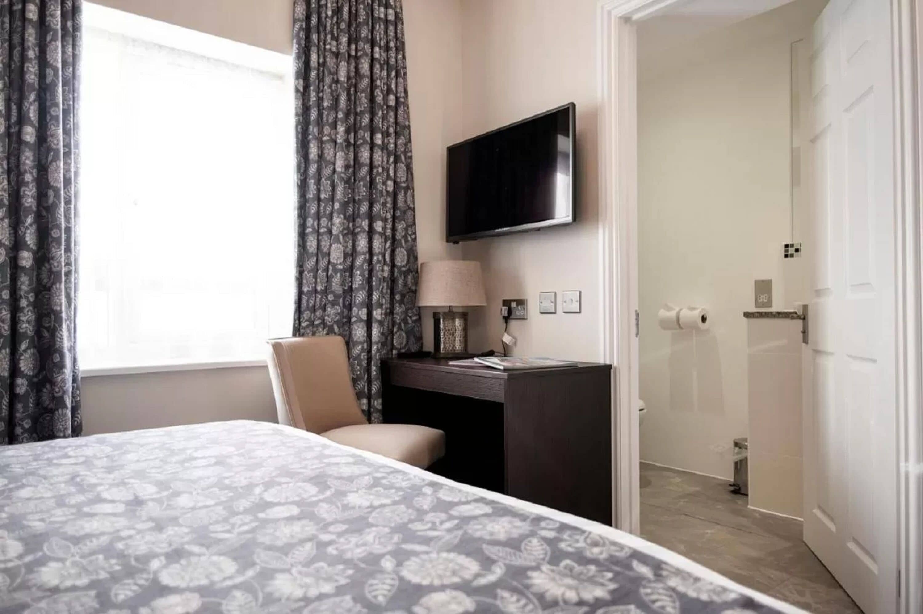 A hotel room with a bed, a desk, a TV, and a bathroom visible through an open door.