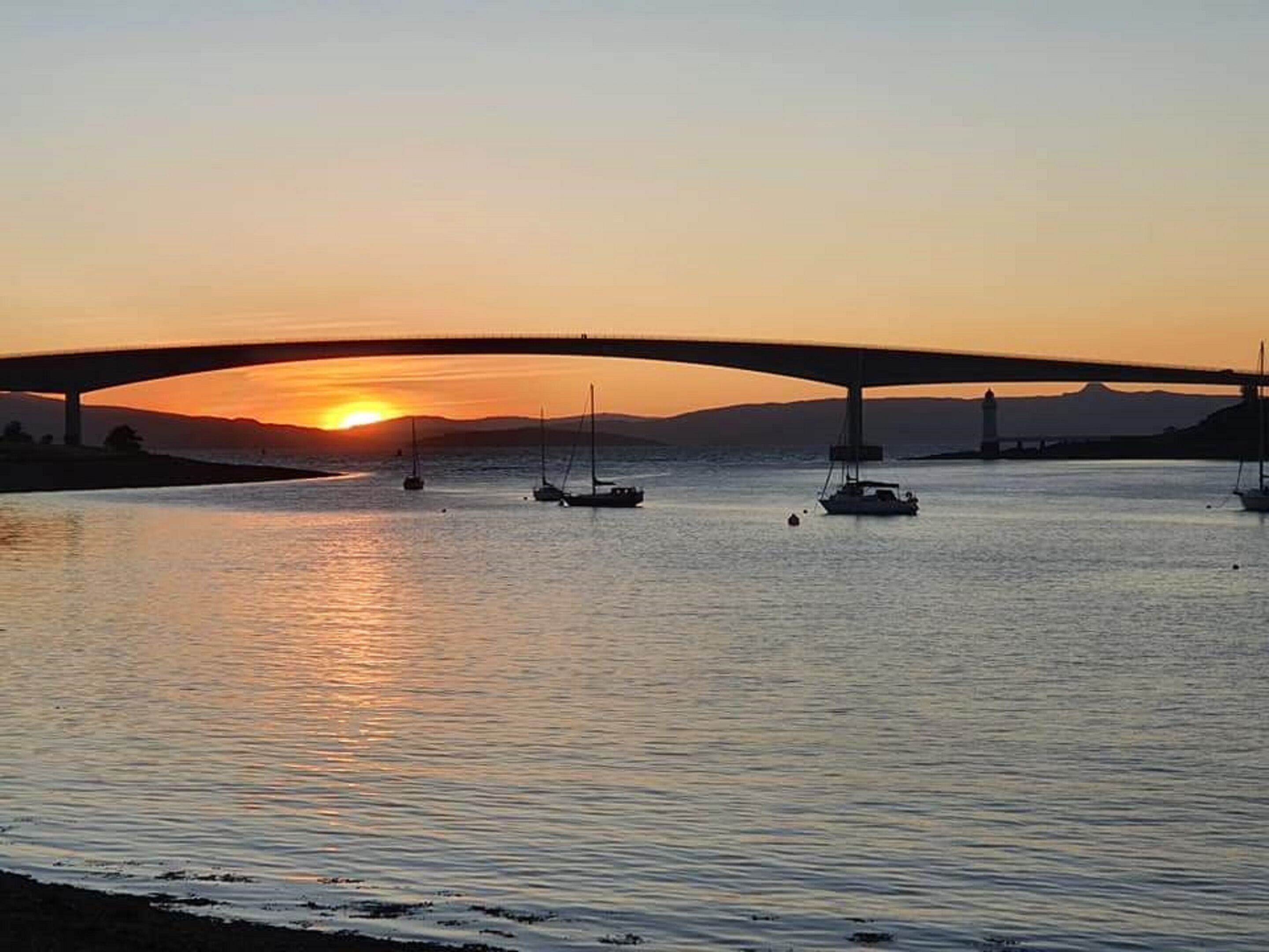 A sunset over a river with boats and a bridge.