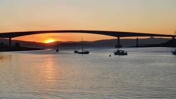 Un coucher de soleil sur une rivière, avec des bateaux et un pont.