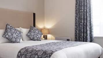 A hotel room with a large bed, a bedside table with a lamp, patterned pillows, and a window with curtains.