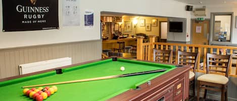 A pool table with balls, a bar area, and wooden chairs.