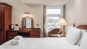 Ein Hotelzimmer mit Bett, Schreibtisch, Stuhl, Lampe, Spiegel und einem Fenster mit Blick auf eine Stadtlandschaft.