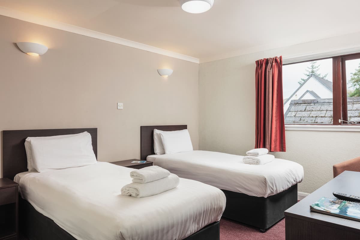 A hotel room with two beds, a desk, and a window with curtains.