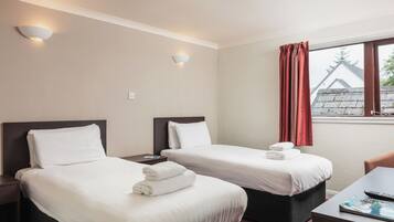 A hotel room with two beds, a desk, and a window with curtains.