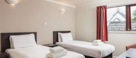 A hotel room with two beds, a desk, and a window with curtains.