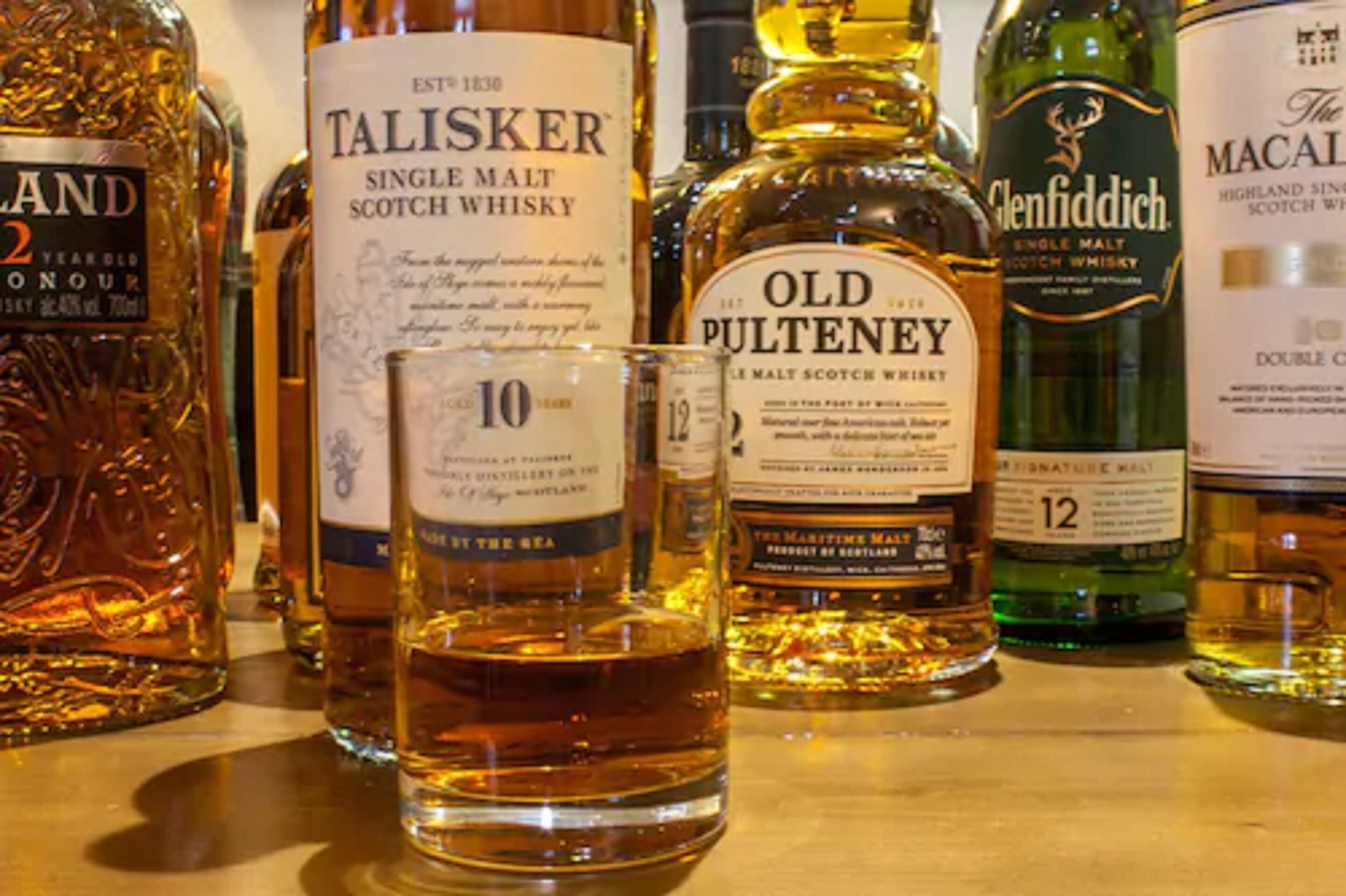 Varias botellas de whisky y un vaso sobre una mesa.