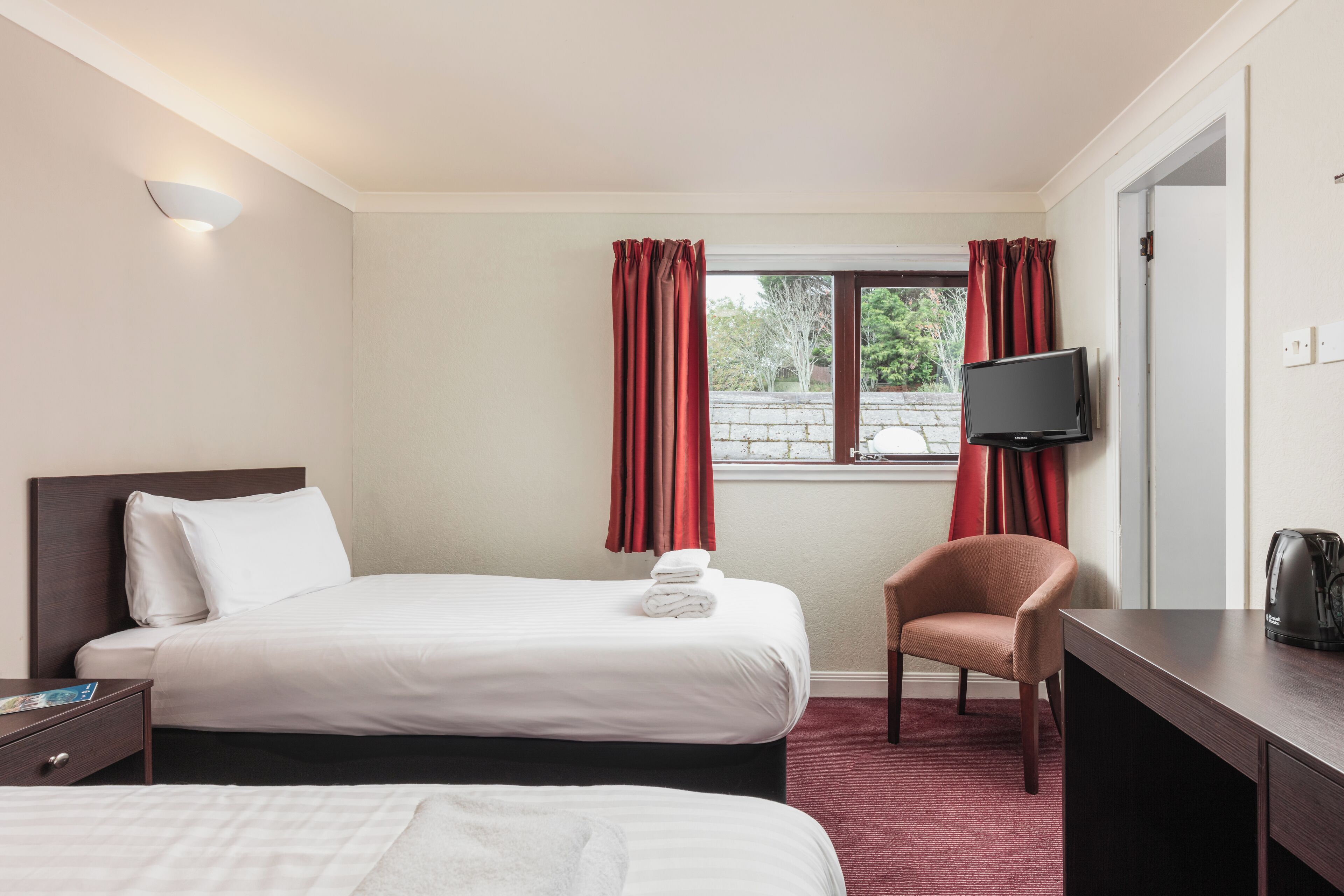 A hotel room with two beds, a TV, a chair, and a desk.