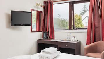 A hotel room with a bed, a desk with a coffee maker, a TV, and a window with curtains.