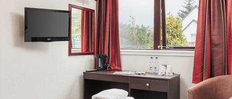A hotel room with a bed, a desk with a coffee maker, a TV, and a window with curtains.
