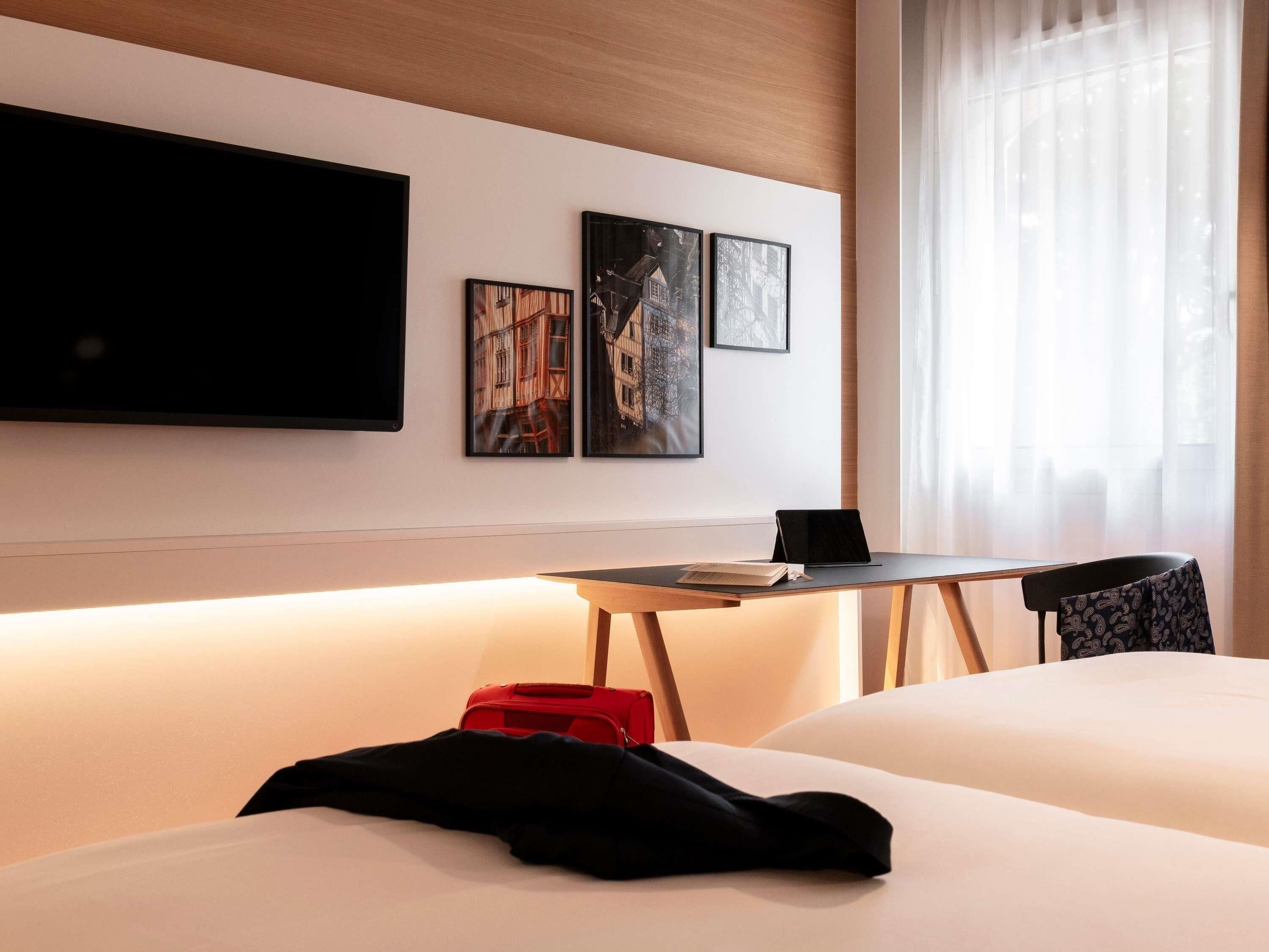 A hotel room with a bed, a desk with a laptop, a chair, and artwork on the wall.