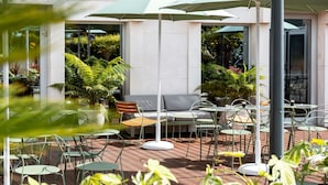 An outdoor patio area with round tables and chairs, a sofa, and umbrellas providing shade. - Hôtel Mercure Rouen Centre Champ-de-Mars (Rouen)