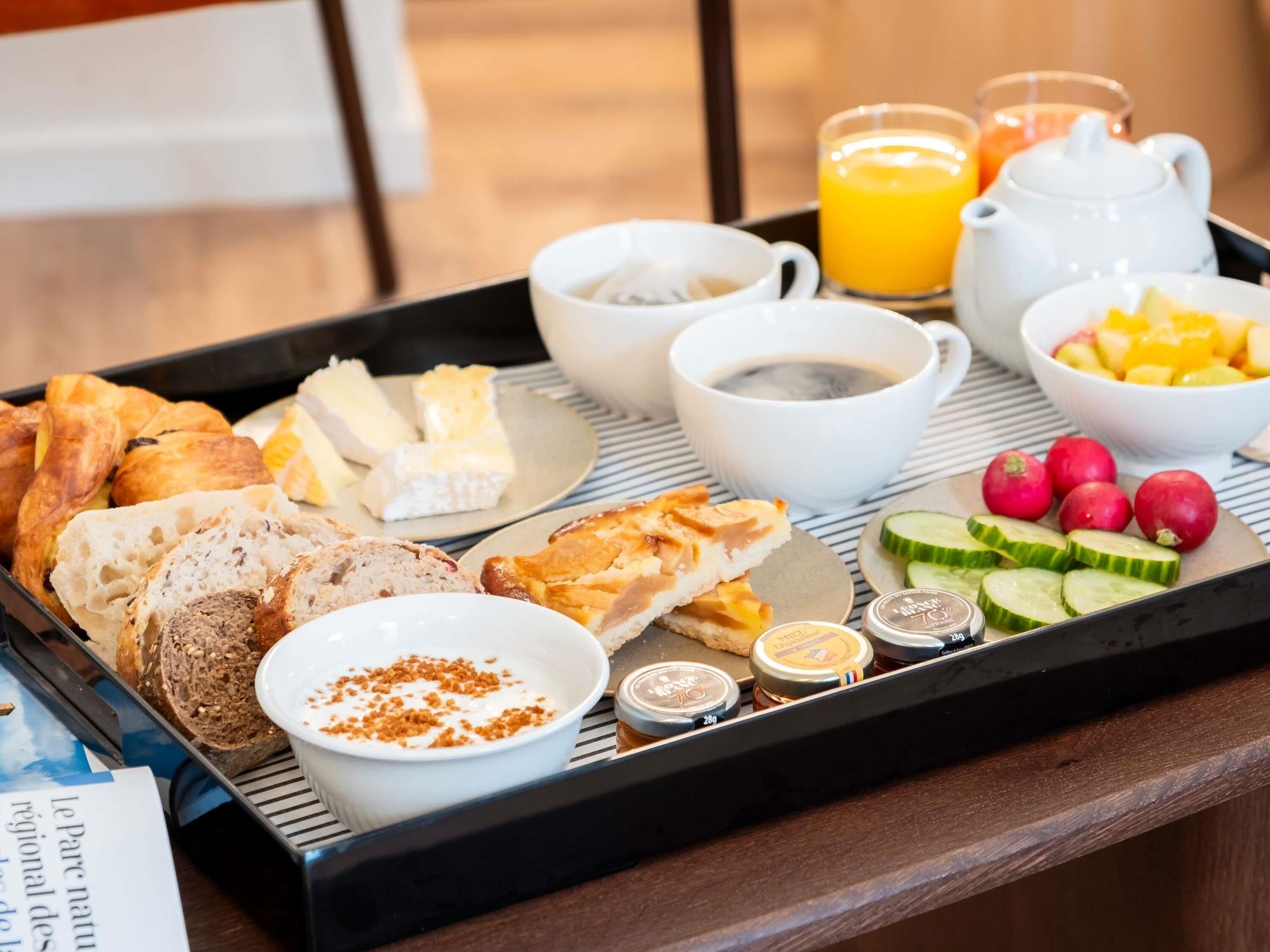 A breakfast tray with croissants, cheese, bread, yogurt, fruit, and condiments.