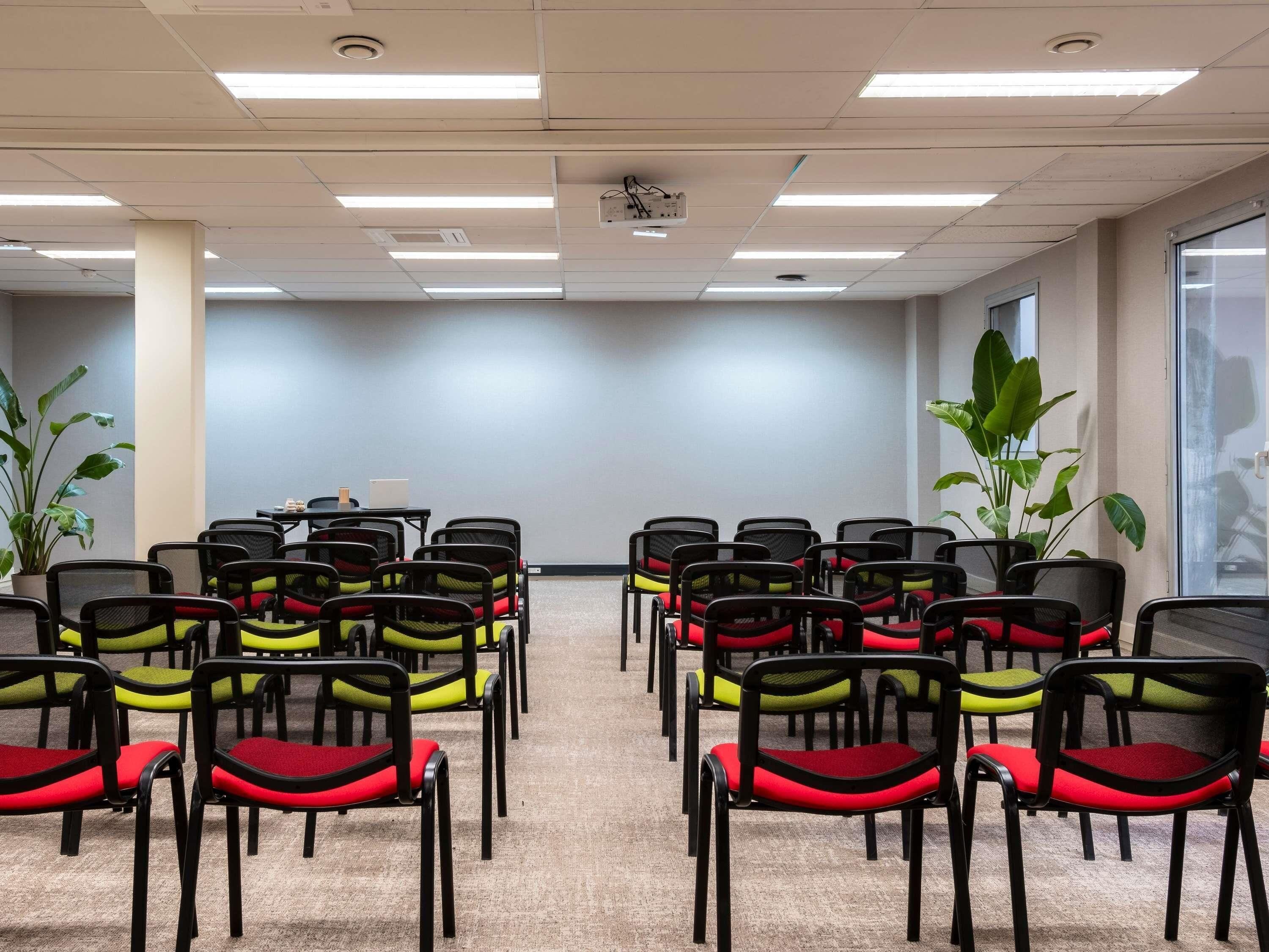Ett konferensrum med rader av stolar, en projektor och en bärbar dator på ett bord.