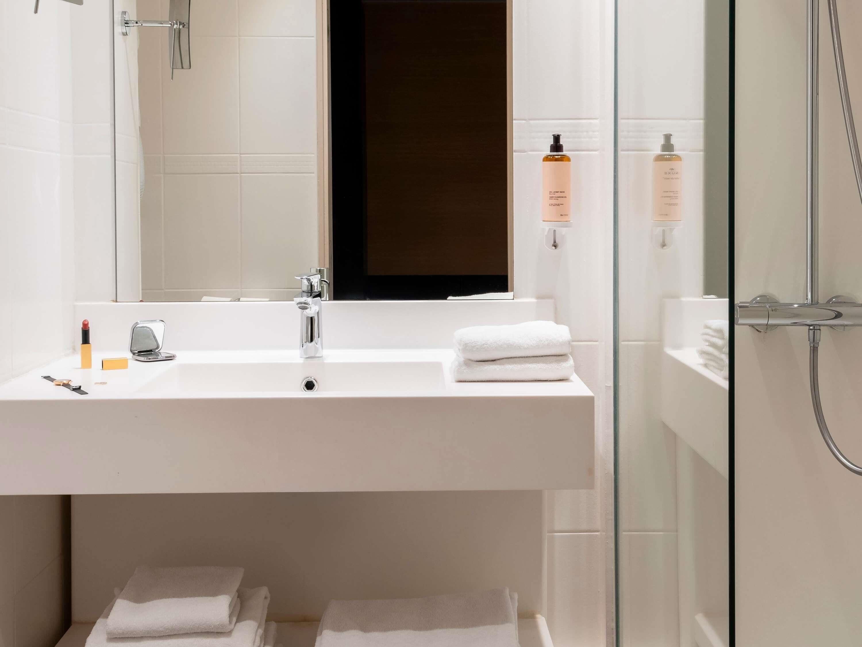 Un baño moderno con lavamanos blanco, espejo y cabina de ducha de vidrio.