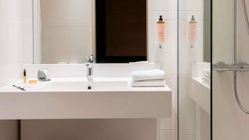 Un baño moderno con lavamanos blanco, espejo y cabina de ducha de vidrio.