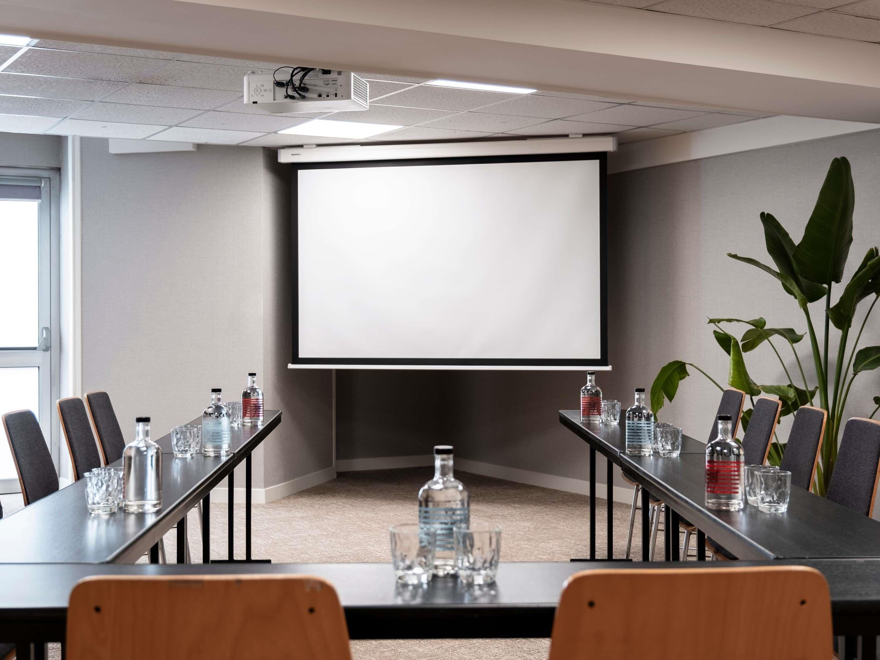 A conference room with a projector screen, a long table with chairs, water bottles, and a potted plant.