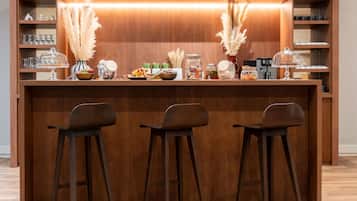Angolo bar con un bancone in legno, tre sgabelli da bar e diversi oggetti, tra cui barattoli e una macchina da caffè.