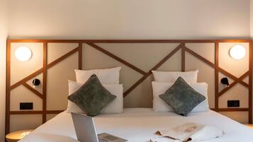 Una cama bien hecha con un ordenador portátil, dos almohadas y una lámpara de noche.