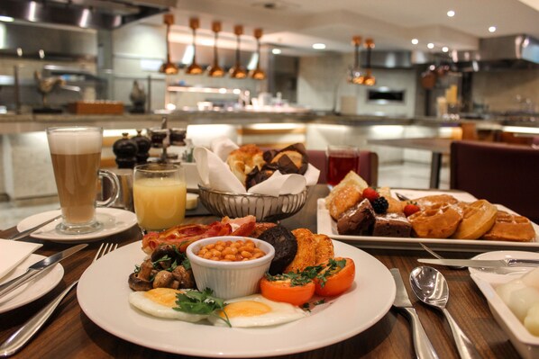 A breakfast buffet with various dishes, a glass of beer, and a bowl of beans.