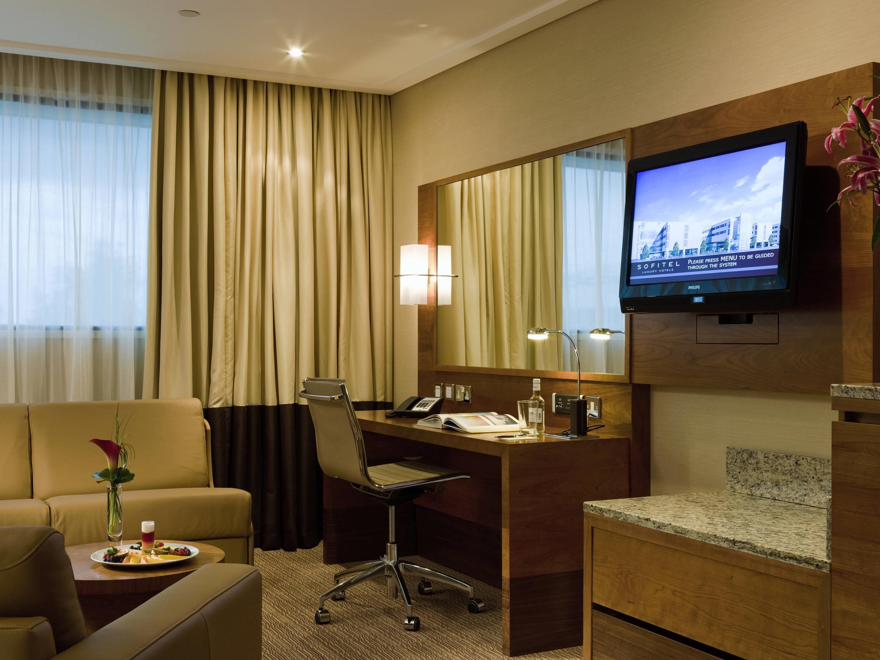 A hotel room with a desk, chair, television, and a view of the cityscape.