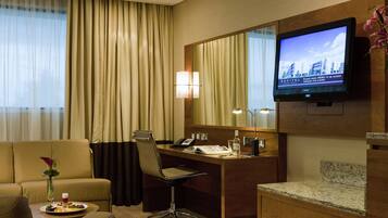 A hotel room with a desk, chair, television, and a view of the cityscape.