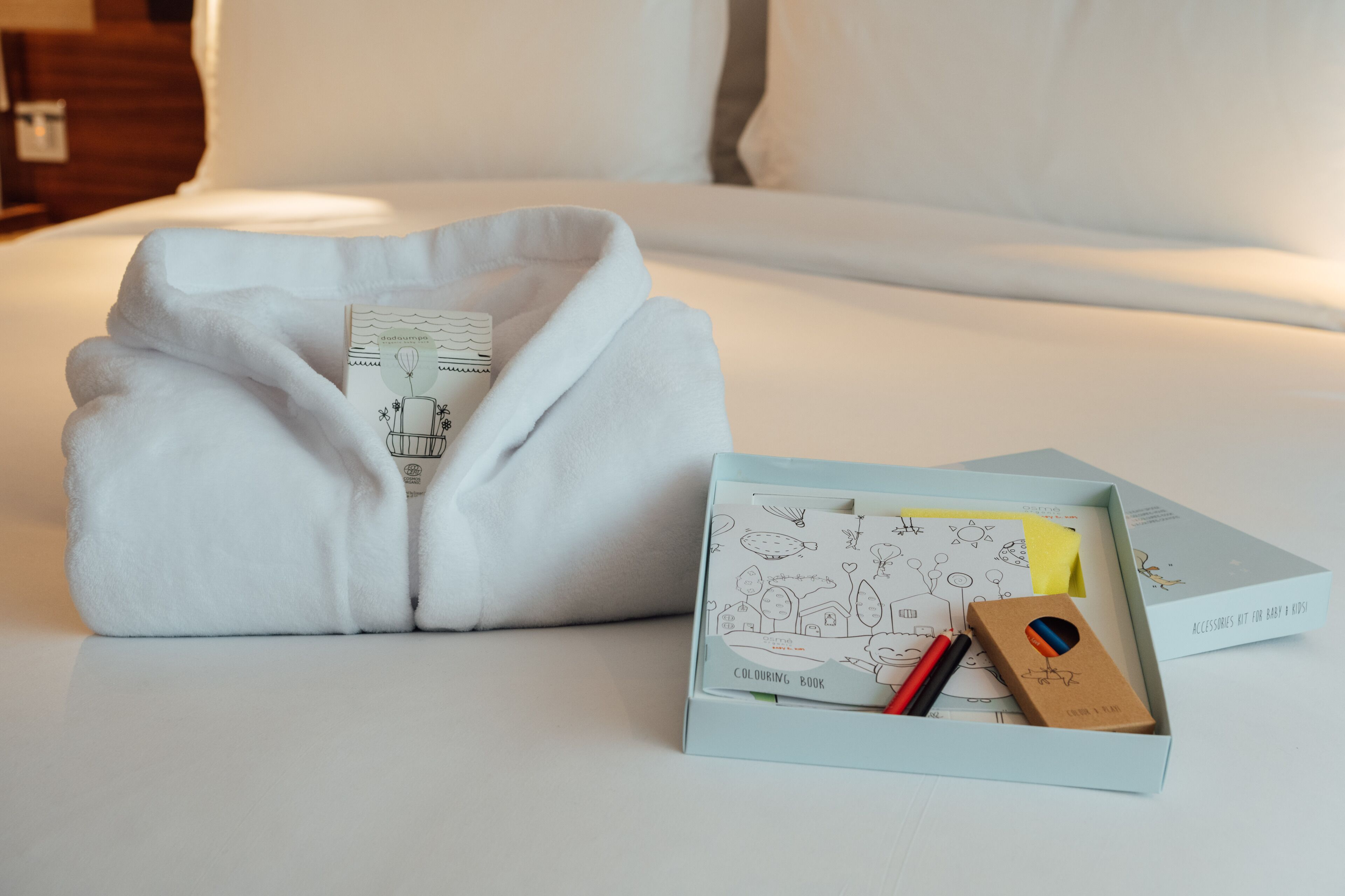 A neatly made bed with a folded white towel and a box of coloring book accessories.
