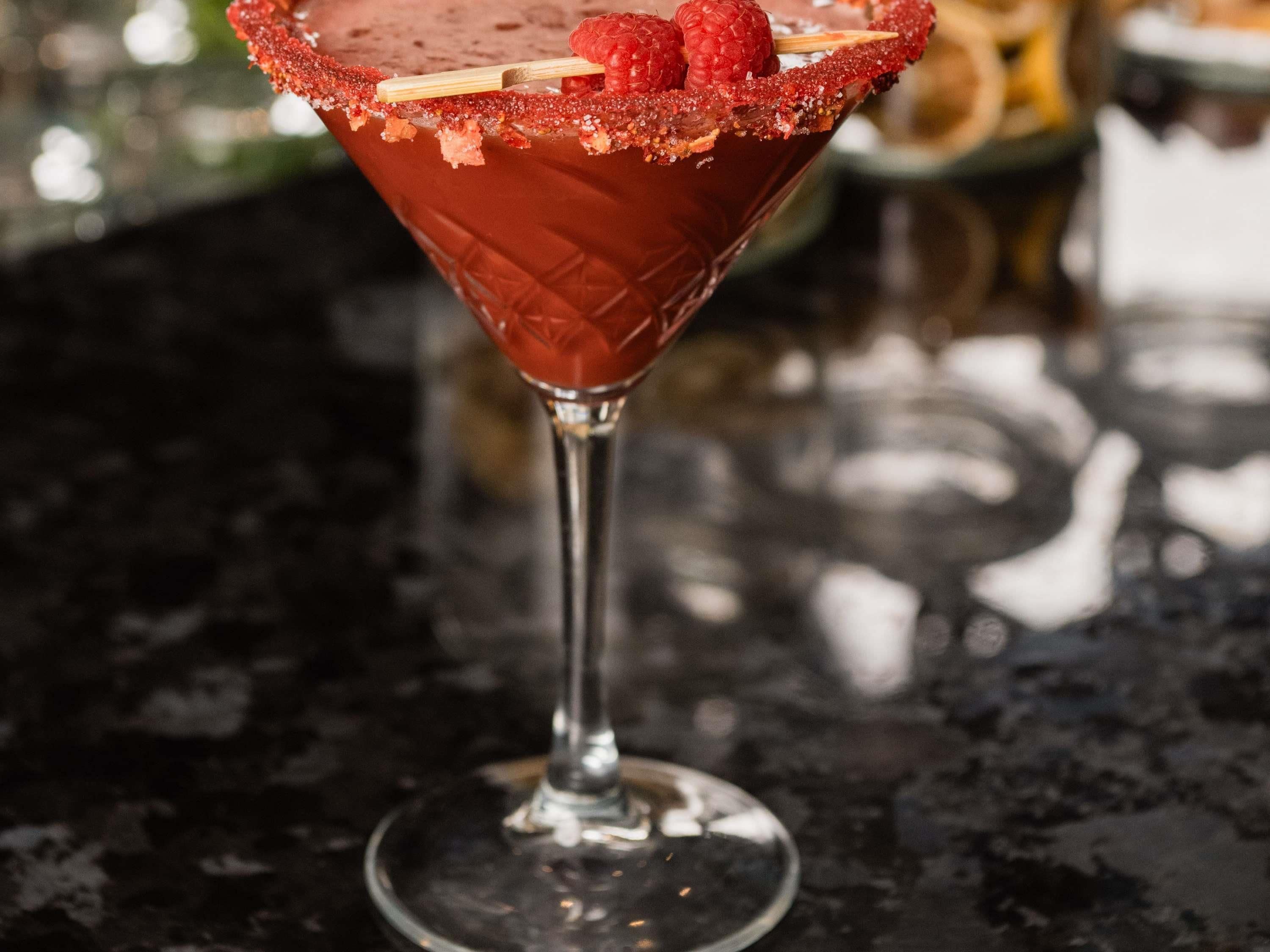 A cocktail with a salted rim and raspberries in a martini glass.