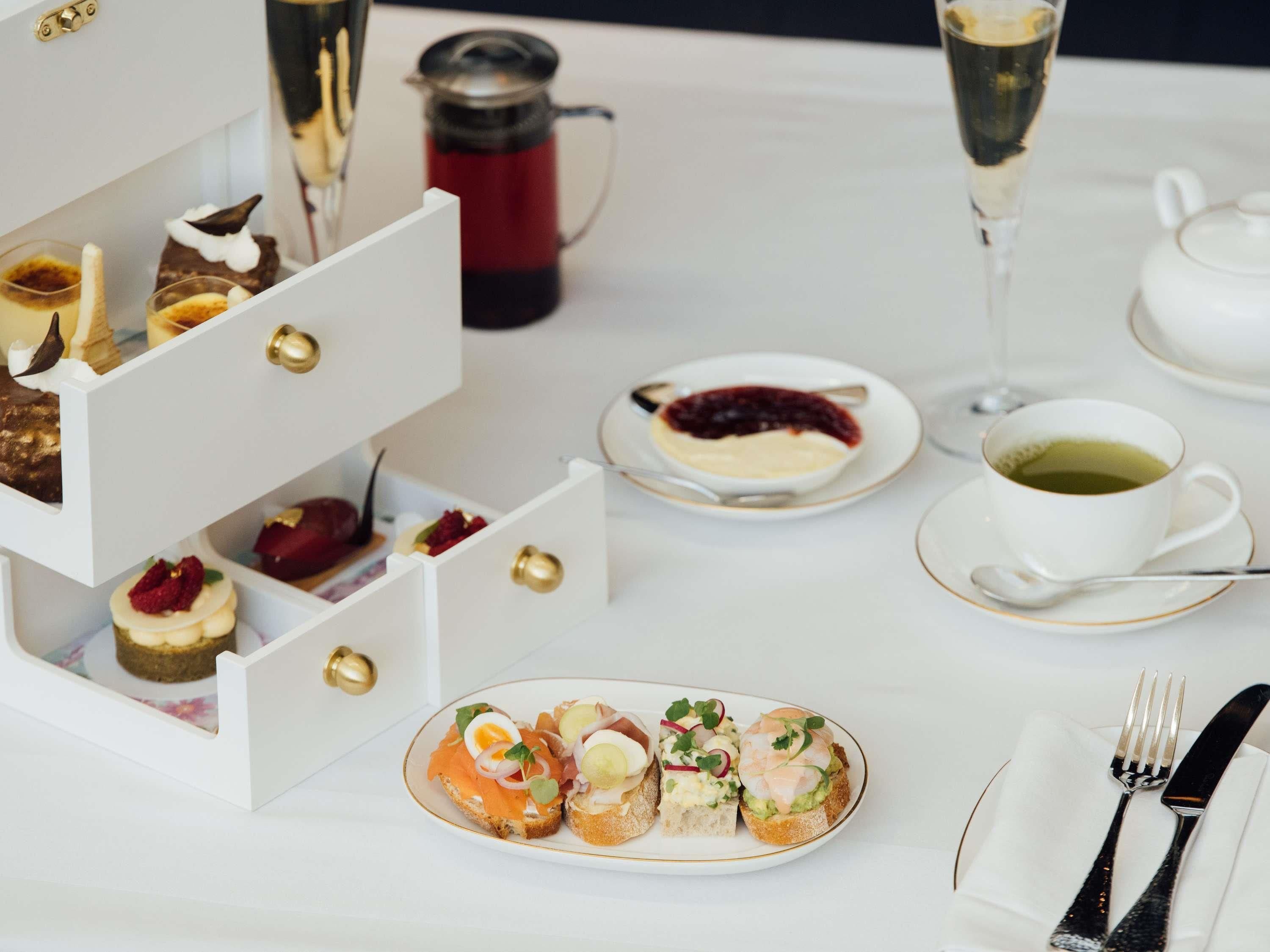 A table set with various food items, including sandwiches and desserts, and a coffee pot.
