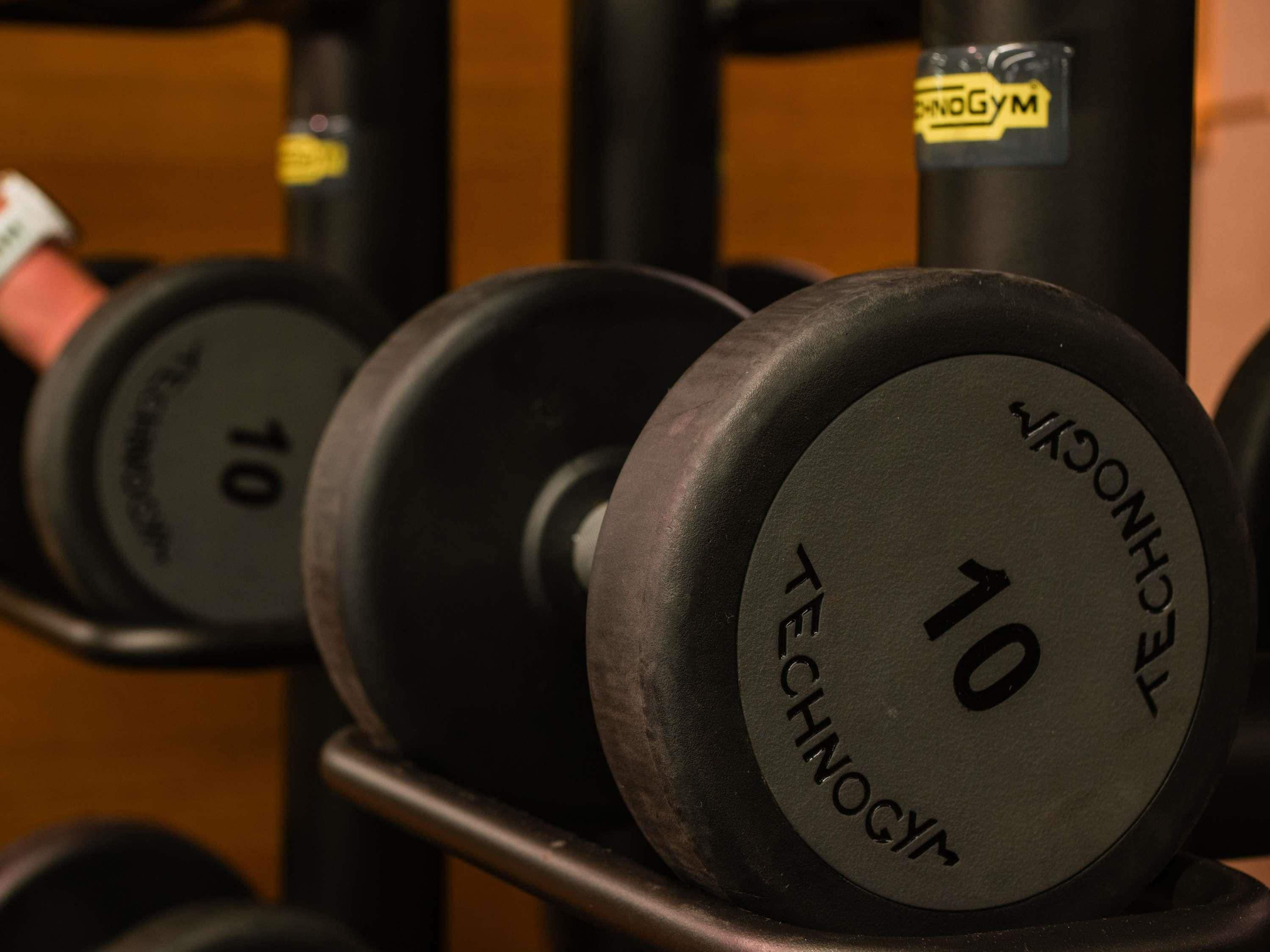 A close-up of a weightlifting dumbbell rack with weights labeled "10" and "TECHNOGYM".
