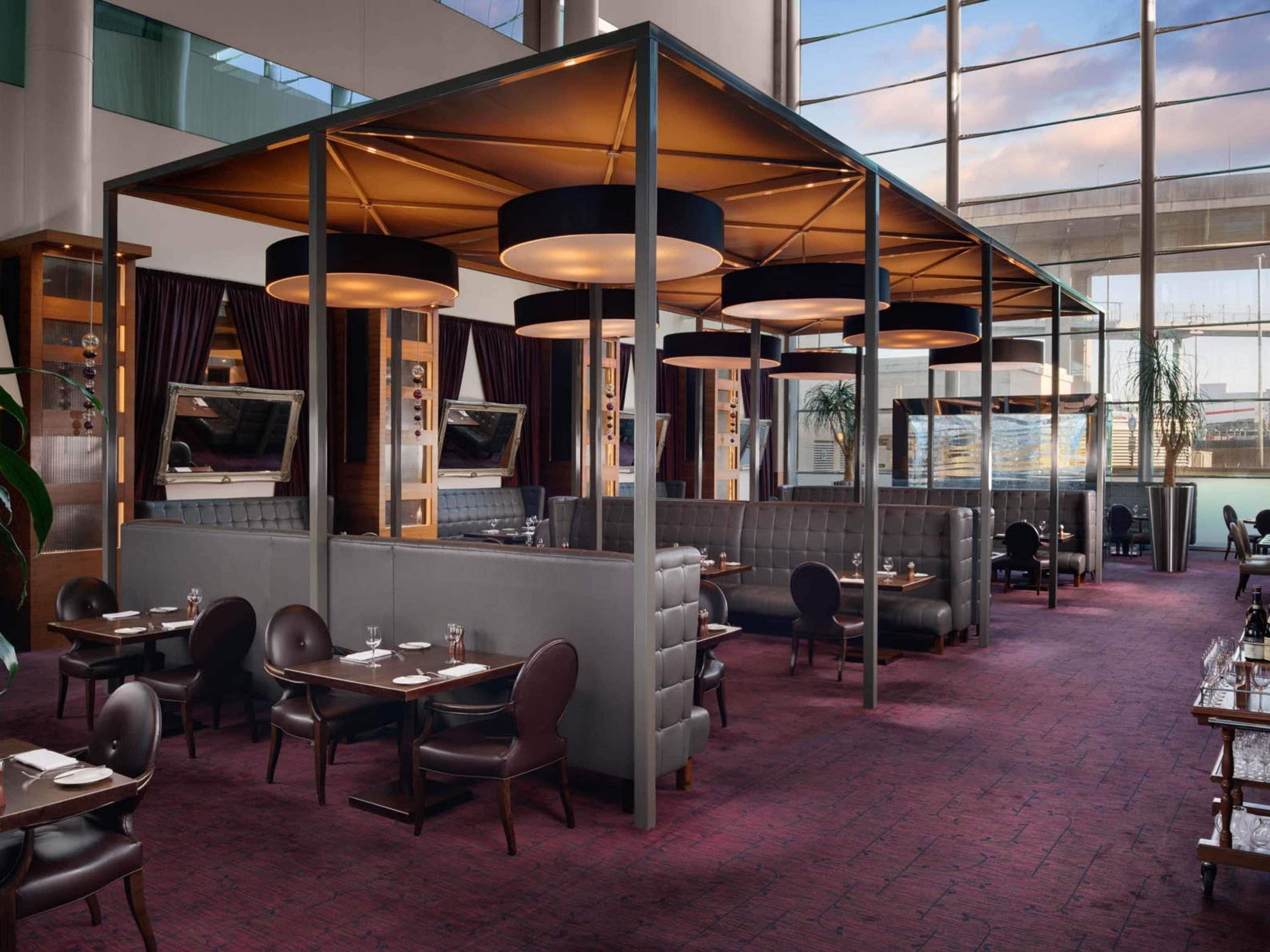 Un restaurante moderno con techos altos, amplios ventanales y una variedad de opciones de asientos, incluyendo cabinas y mesas.