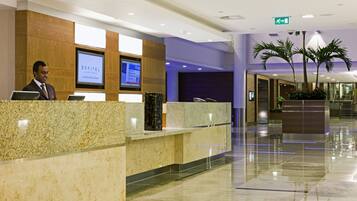 A hotel reception area with a modern design, featuring a reception desk, digital screens, and a well-lit interior.