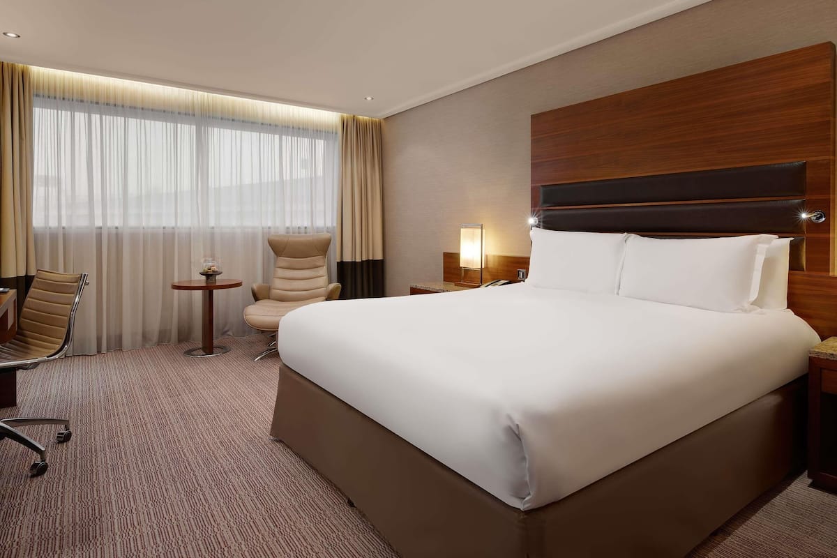 A hotel room with a large bed, a chair, a small table, and a lamp.