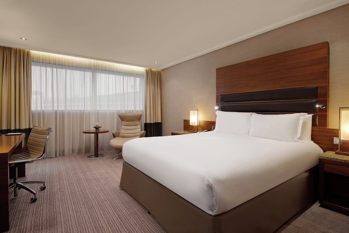 A hotel room with a large bed, a desk, a chair, and a small table.