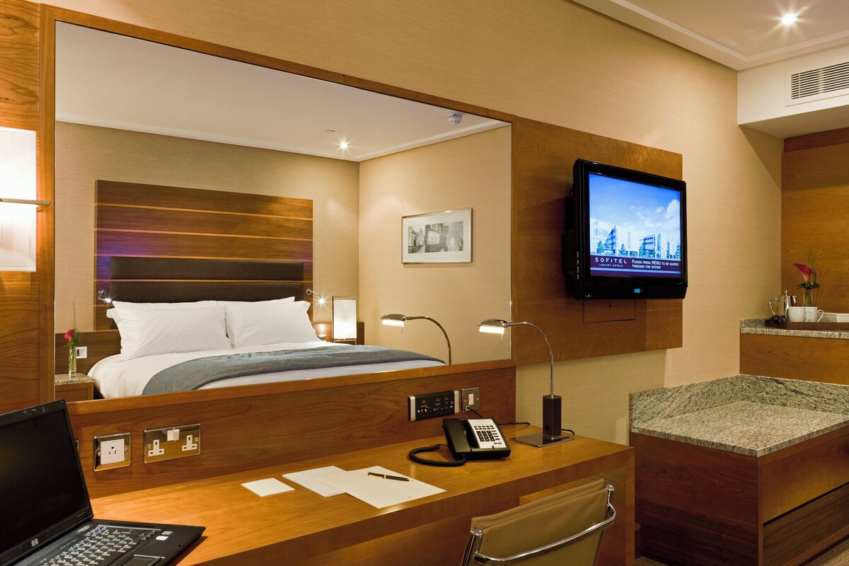A hotel room with a bed, a desk with a laptop, a telephone, and a television mounted on the wall.