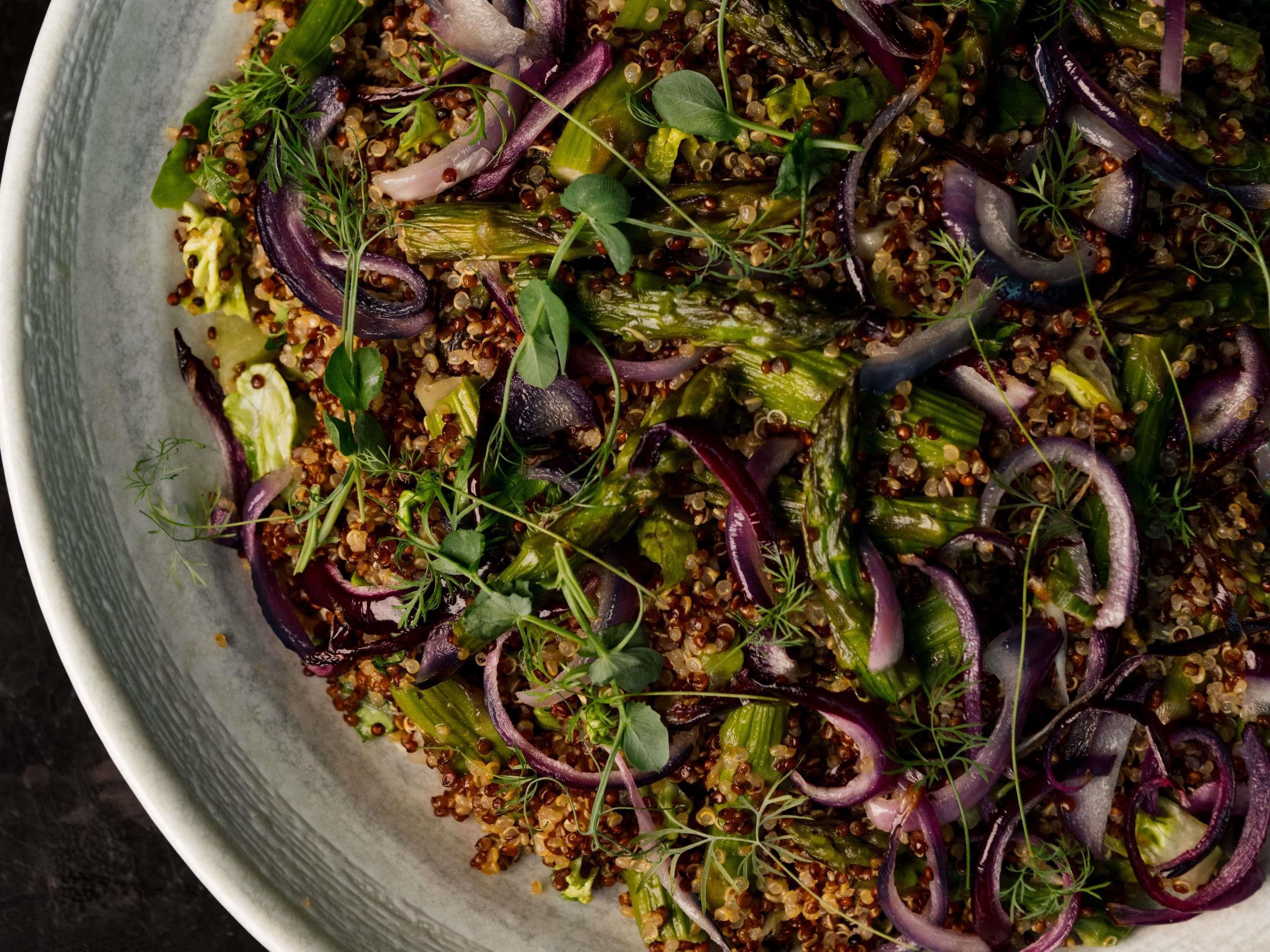 A bowl of quinoa salad with mixed vegetables and herbs.