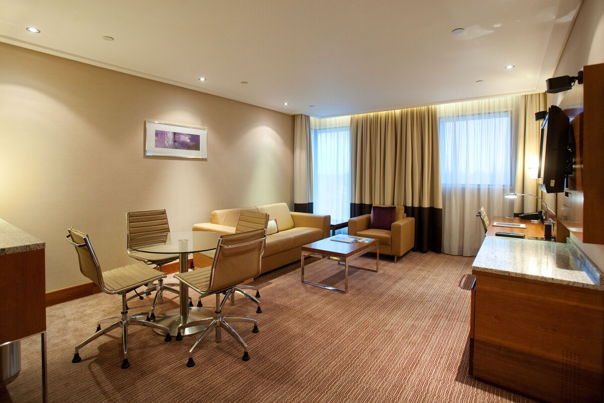 A hotel room with a dining area, a sofa, a coffee table, and a TV.