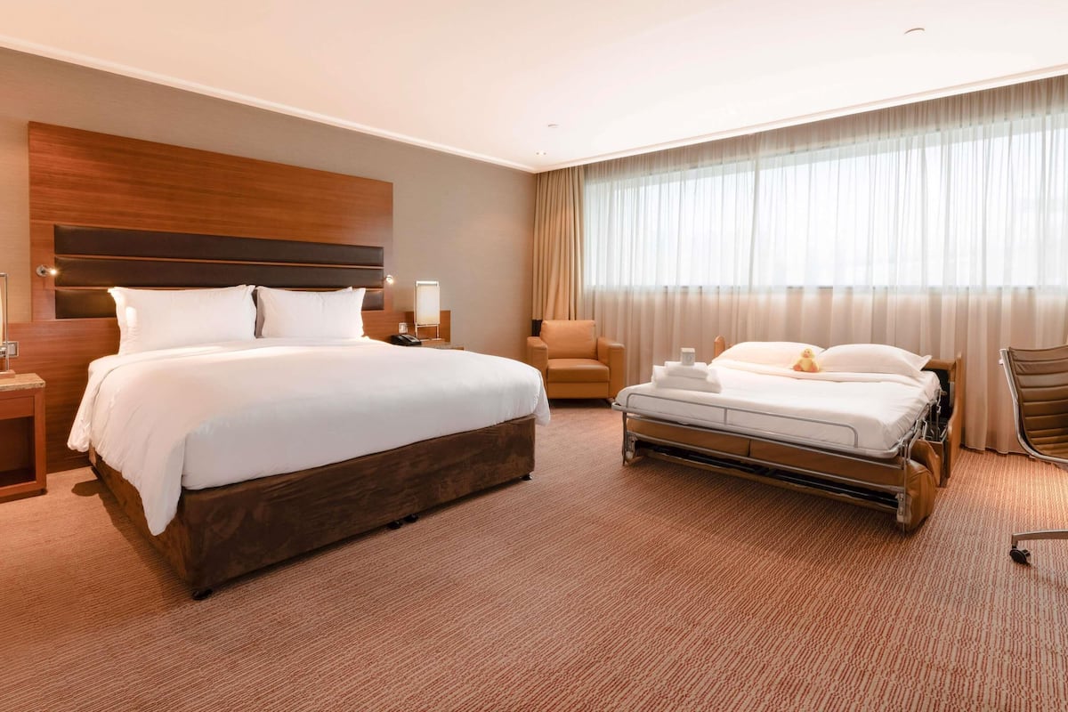A hotel room with a large bed, a smaller bed, a chair, a desk, and a window with curtains.