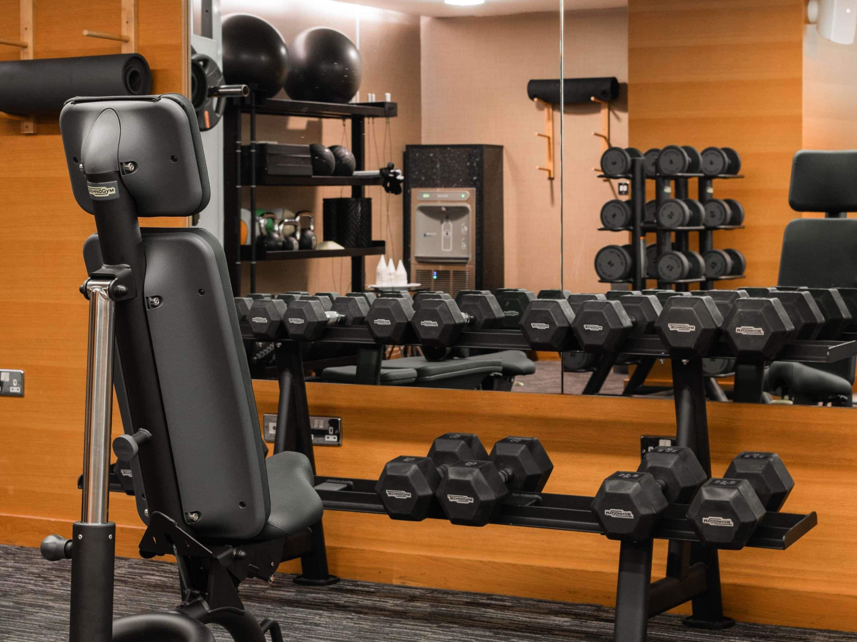 Un gimnasio con diversos equipos de ejercicio, incluyendo mancuernas, una banca y una máquina de remo.