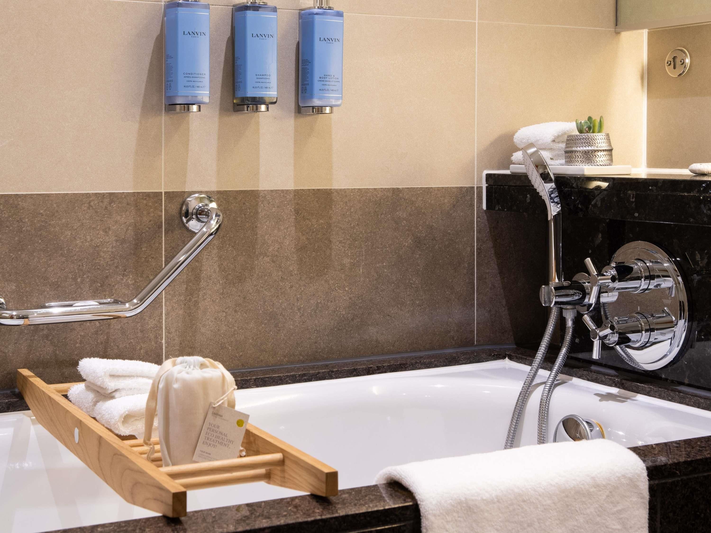 Ein Badezimmer mit einer Badewanne, einer Dusche und drei Flaschen Lanvin Produkten an der Wand.