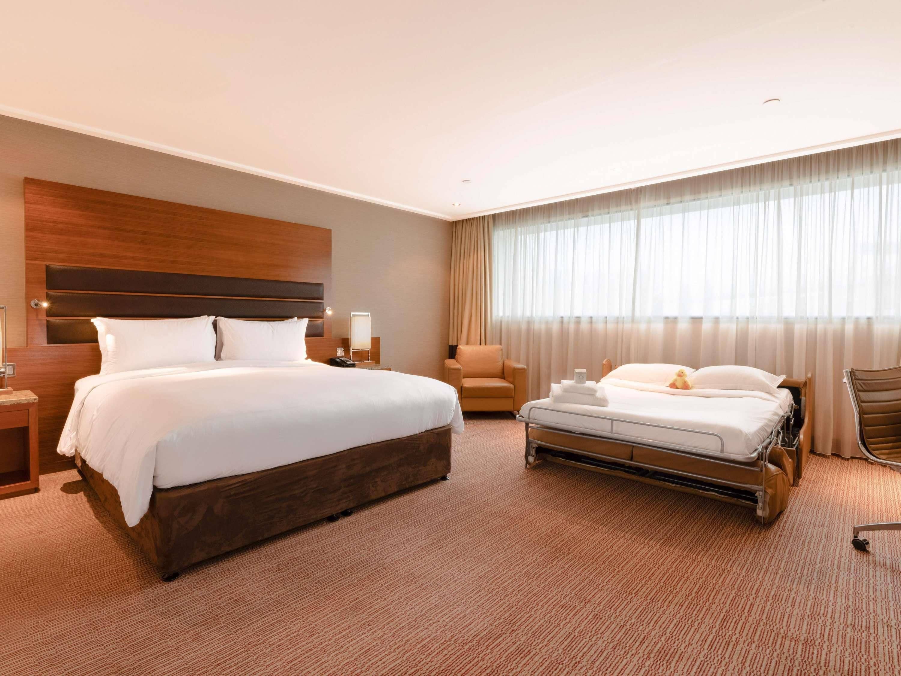 Habitación de hotel con una cama grande, una cama más pequeña, una silla, un escritorio y una ventana con cortinas.