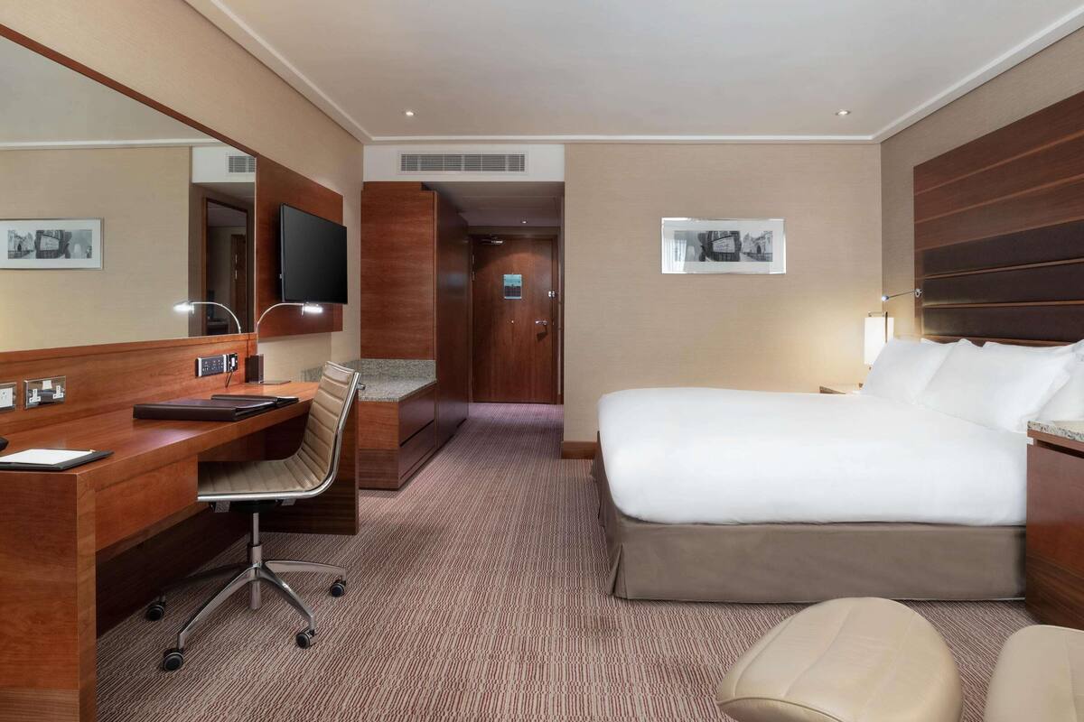 A hotel room with a bed, desk, chair, and a television.