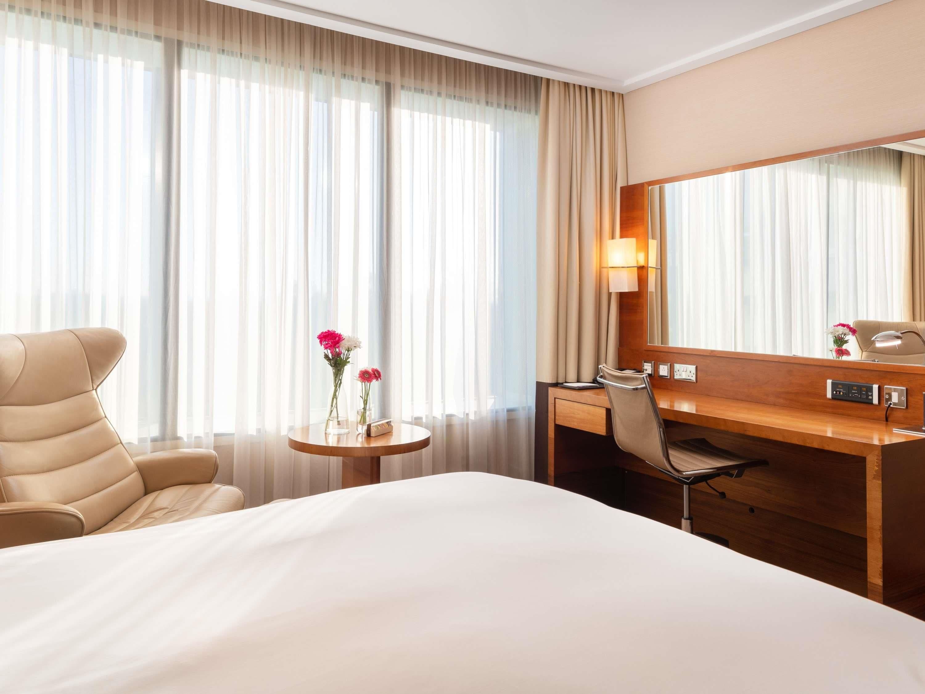 Habitación de hotel con una cama grande, un escritorio con silla, una mesita con flores y un espejo amplio.
