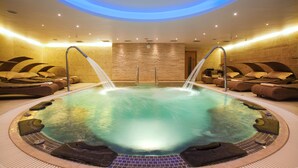 Een hottub met twee waterstralen, omringd door lounge stoelen en een betegelde vloer.