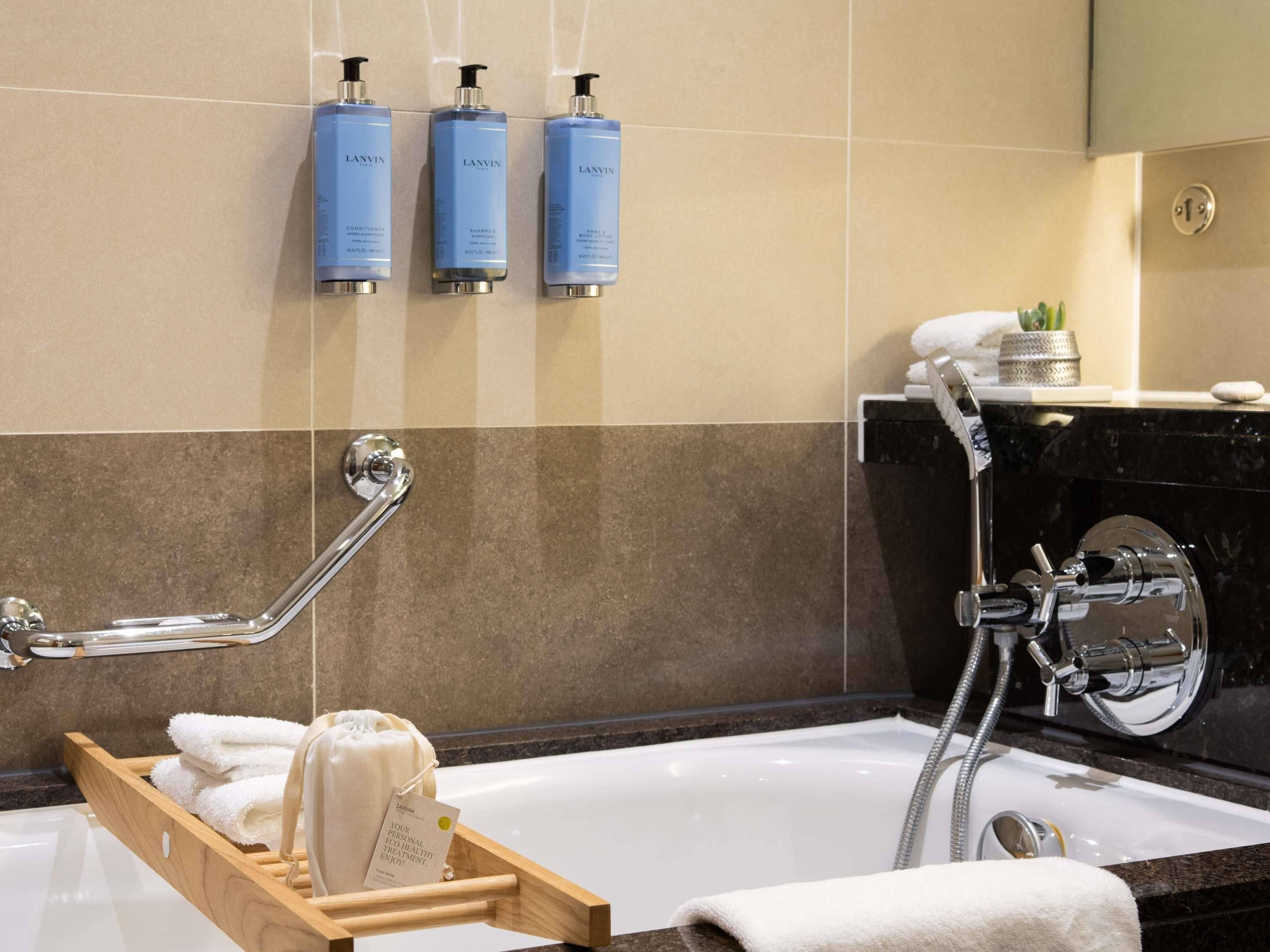 Une salle de bain moderne avec une baignoire, un porte-serviettes en bois et trois produits de toilette de la marque Lanvin accrochés au mur.