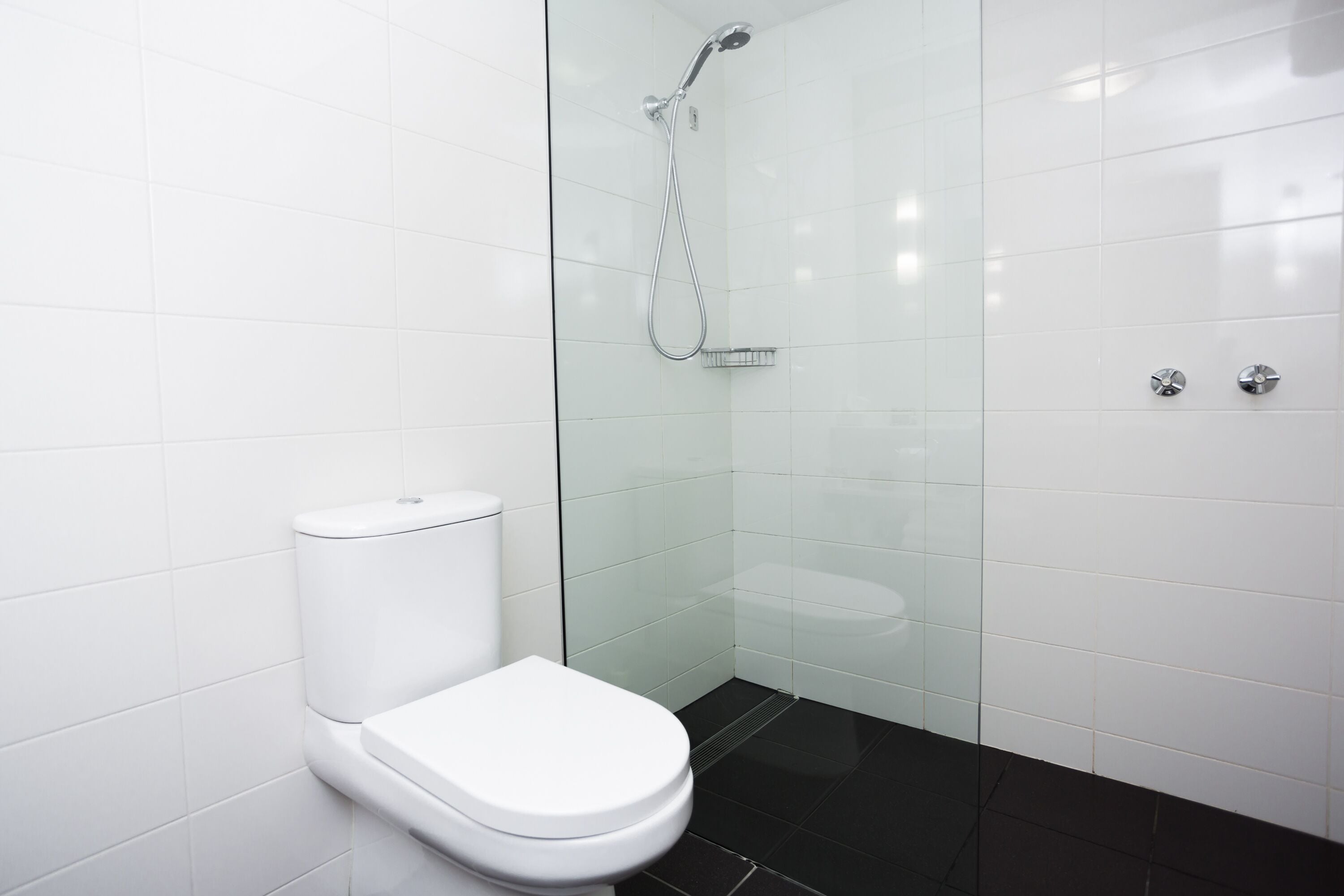 Une salle de bain moderne avec des toilettes blanches, une douche en verre et un sol carrelé de couleur noire.